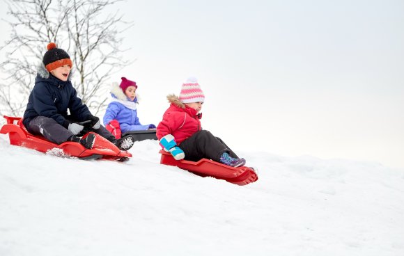 kids sliding on sleds down snow hill in winter