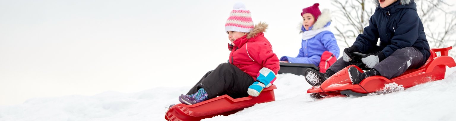 kids sliding on sleds down snow hill in winter